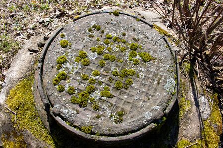 old sewer manhole covered in moss on the green lawn.