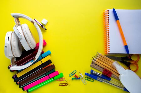 Lots of different office supplies and white headphones on a yellow background. Close-up, copy space,...