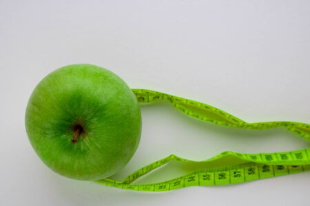 an Apple and a centimeter-long ribbon on a white background with a place to insert text. minimalism. concept of diet, healthy eating, fat burning, caloriesの写真素材
