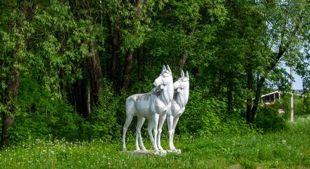 Sculpture of two white moose on the background of a green forest, on the outskirts of a provincial townの写真素材