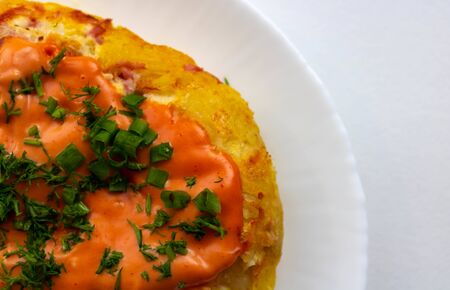 A portion of potato casserole with sauce and herbs on a white plate