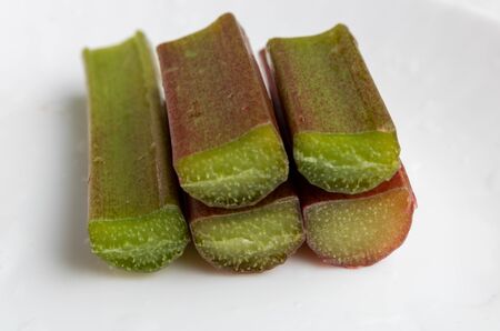 A bunch of red-green rhubarb stalks with water drops on a white background