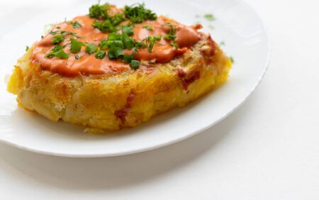 A portion of potato casserole with sauce and herbs on a white plate.