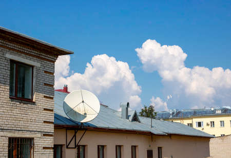Clouds and a TV antenna. white satellite dish on the roofの写真素材