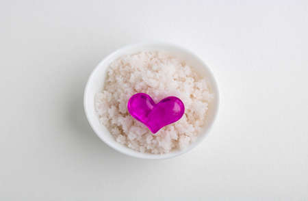 An oval white bowl with pink salt and a pink heart stands on a white background.の写真素材
