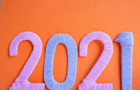 The numbers 2021 are made of pink and lilac threads on an orange background. The concept of a New year.の写真素材