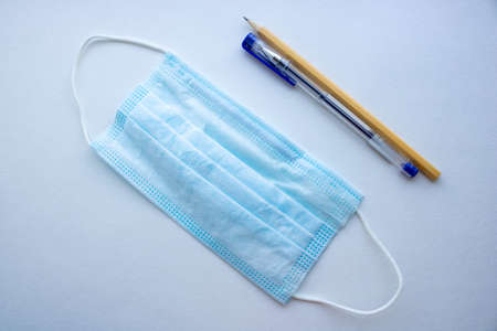 A surgical or medical mask with rubber ear straps lies next to a pen and pencil on a white background. A typical 3-layer doctor's mask to cover your mouth and nose.の写真素材