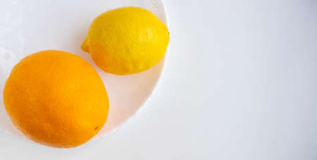 One lemon and an orange lie on a white plate, isolated on a white background. Tropical fruit. Flat bed, top viewの写真素材