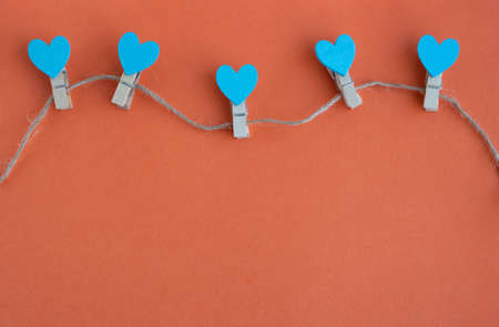 Small clothespins and blue hearts on a rope on an orange background.の写真素材