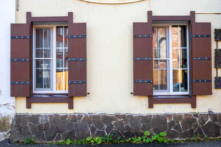 Two Windows with wooden shutters on the pink facade of a residential building.
