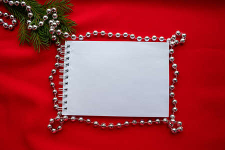 Composition - Notepad and green spruce branches with silver beads on a red background. New year's...