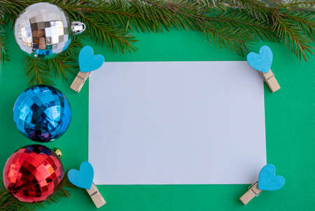 New year's composition.Spruce branches with balloon toys, clothespins with hearts and a white blank sheet. Space for your text.の写真素材