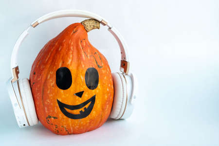 Funny pumpkin with headphones on a white background. The concept of Halloween, harvest, thanksgiving, vegetarianism. Space for your text.の写真素材