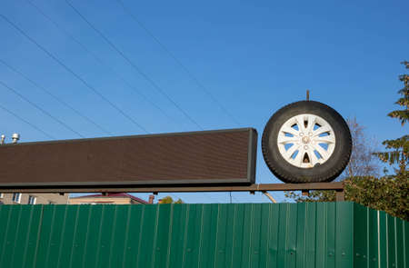 Metal fence construction: green corrugated steel fence with scoreboard and wheel under blue sky.の写真素材