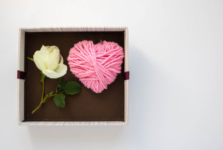 Gift brown box with a knitted heart and a white rose on a white background. Concept of Valentines Day, anniversary, mothers Day, March 8 and birthday greetings. Space for your textの写真素材