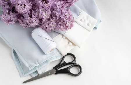 Old scissors, a spool of thread, a cloth and a branch of lilac shot in a nostalgic tone.