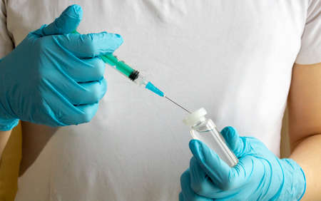 Blue-gloved hands fill a syringe with the vaccine. The concept of medicine and healthcare.
