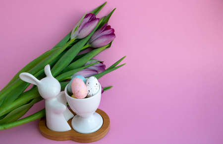White rabbit, Easter eggs and lilac tulips on pink background, Easter celebration concept.