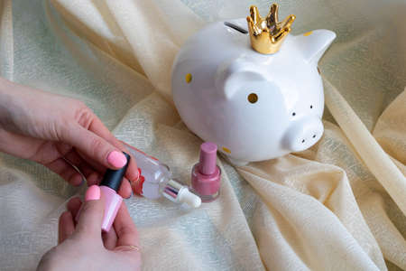 White piggy bank-piggy and female hands with pink nail design. Pink shiny nail polish manicure....
