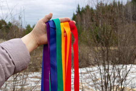 The concept of Valentine's Day, freedom, love. A hand holding rainbow ribbons on the background of a spring river.の写真素材