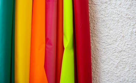Rolls of multicolored fabric stand against the wall. Space for your text.