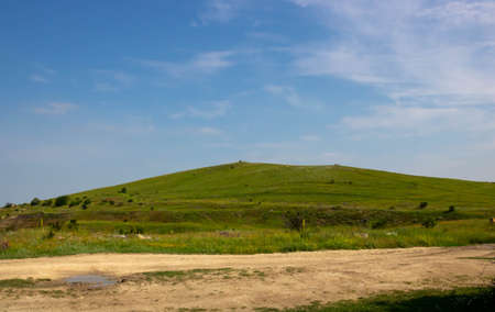 A green hill and a dirt road on the background of a blue sky with clouds.