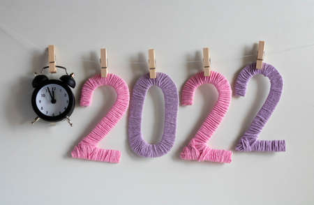 The clock and the numbers 2022 made of pink and lilac threads on a white background hang on clothespins. The concept of the New Year.の写真素材