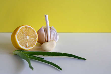 Composition with natural cold remedies on a white table on a yellow background. Garlic, lemon, aloe folk remedies against the autumn cold, covida.の写真素材