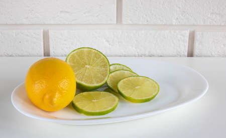 Lime, lemon - Juicy ripe citrus fruits on a white plate on a kitchen background. Ingredients for making refreshing drinks and Mojito cocktails. Place for your text.の写真素材