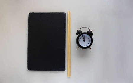 A black slate plate with chopsticks and a black alarm clock. A plate of sushi on a white table. Place for textの写真素材
