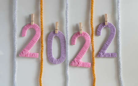 On the clothespins hang the multicolored numbers 2022 on a white background with shiny tinsel. The...