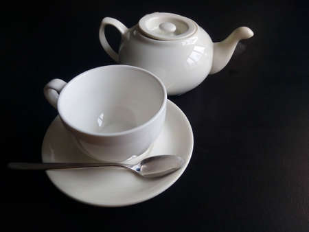 White cup and saucer and teapot isolated on black background.