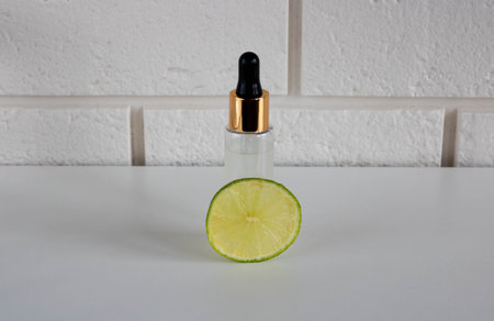 Essential oil in a glass dropper bottle and a fresh piece of lime fruit, highlighted on a white...