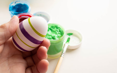 The hand holds a white egg for coloring. The process of painting an Easter egg with light green paint. The tradition and concept of Easter. Spring season, April holidaysの写真素材