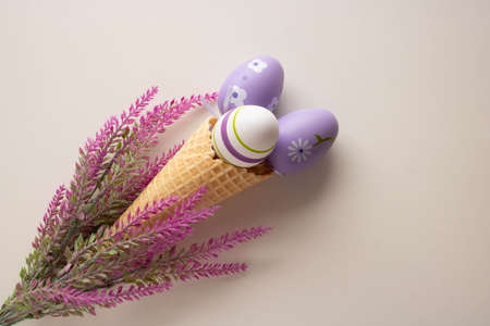 Easter composition, a branch of artificial lavender and three eggs in a waffle cone on a white...
