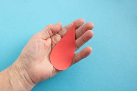 The concept of the World Blood Donor and Hemophilia Day. Red paper drop of blood in the hand on a...