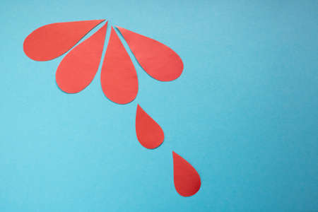 The concept of the World Blood Donor and Hemophilia Day. Red paper drops of blood on a blue...