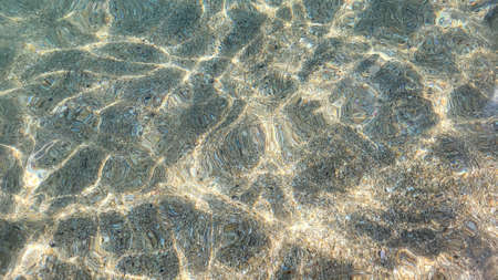 Sea sandy bottom is visible through clear turquoise sea water. Sun glare on sea surface. Beautiful...