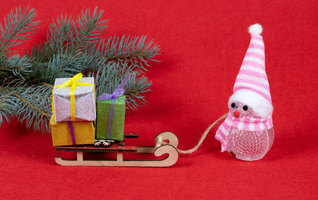 Christmas composition: funny snowman with gifts on a sled in fir branches. New Year 2023.
