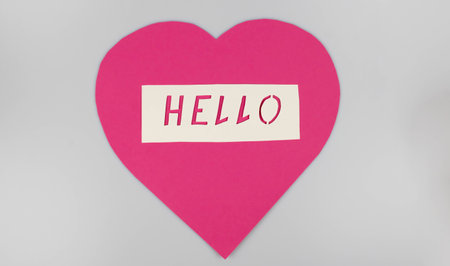 World Greetings Day. The day of winning friends. The word hello and a pink heart cut out of paper on a white background. The concept of communication.の写真素材