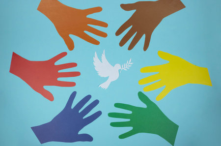Multicolored paper hands reach for a paper pigeon on a blue background. world peace day. World...