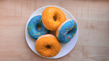 Orange and blue donuts are on a white plate on the tableの写真素材