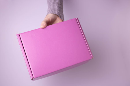 The hand holds a pink gift box closed.