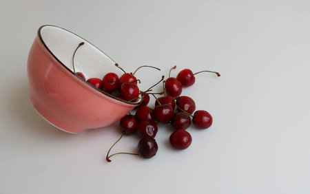 Fresh beautiful cherries from a pink bowl spilled onto the table.