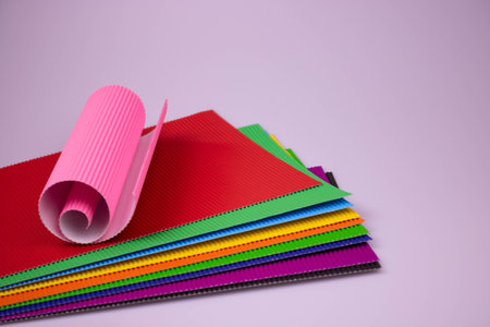 A roll of pink corrugated paper on multicolored leaves of corrugated paper.の写真素材