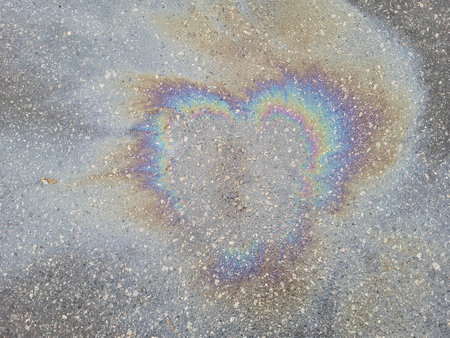 An oily rainbow spot in the shape of a heart on wet asphalt. The concept of ecology. Valentine's day.の写真素材