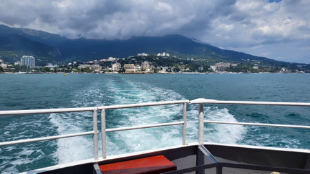 The trail of a pleasure boat on the sea, the coast of the resort city of Yalta, stretching into the distance on a cloudy day with clouds in the sky.の写真素材