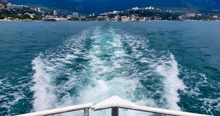The trail of a pleasure boat on the sea, the coast of the resort city of Yalta, stretching into the distance on a cloudy day with clouds in the sky.の写真素材