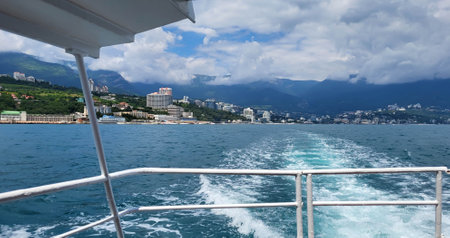 The trail of a pleasure boat on the sea, the coast of the resort city of Yalta, stretching into the distance on a cloudy day with clouds in the skyの写真素材