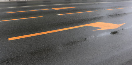 A wet road with yellow arrows on the asphaltの写真素材